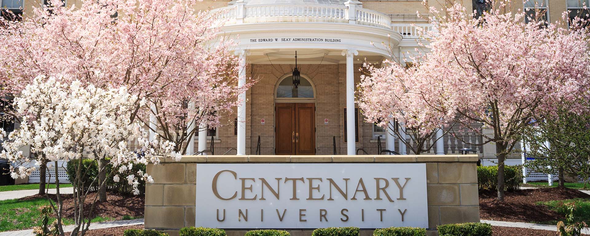 careteam centenary university sign infront of the edward seay administration building with cherry blossom trees