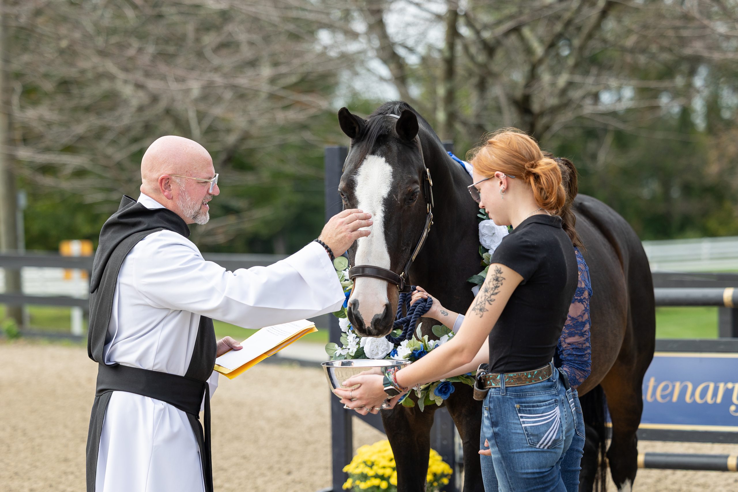A man blesses a black and white horse whose bridle is held by a red-headed woman.
