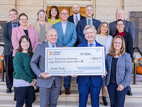 A group of diverse people stand in front of a building in several rows, and the front row of people hold a large check for $8,500.